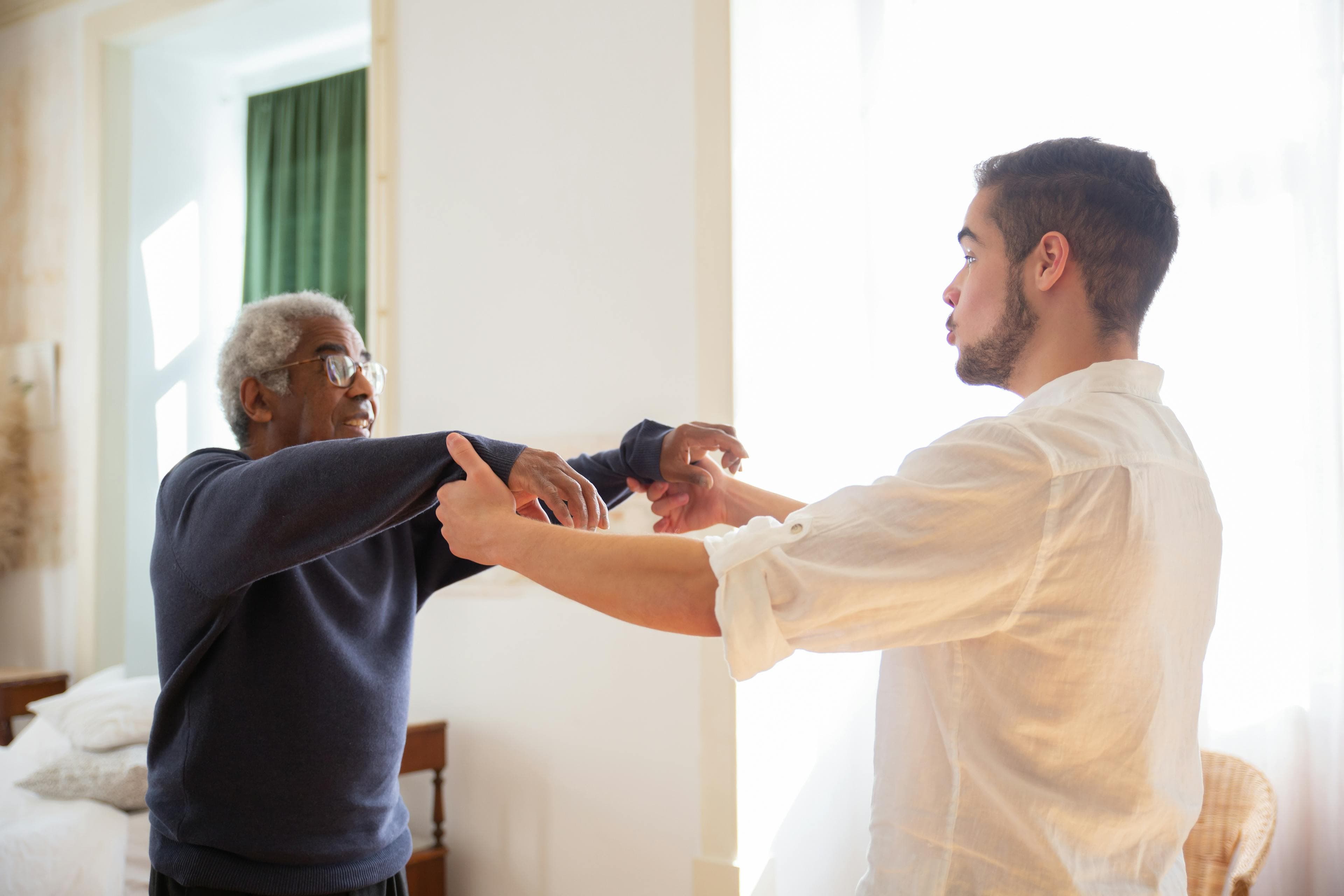 A caregiver holds hands with an elderly man at home, offering reassurance during recovery